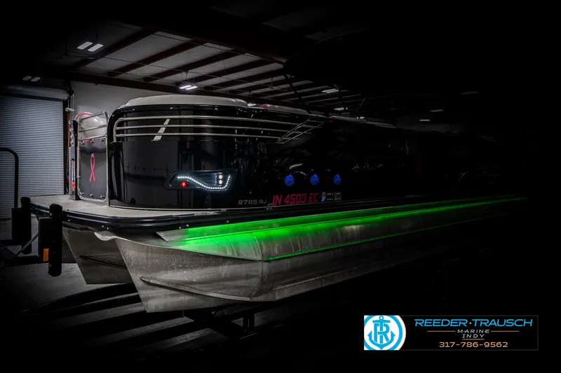 Slide: The Image of 2019 Avalon Ambassador 27' pontoon boat with green LED lights in a dimly lit warehouse. - 4
