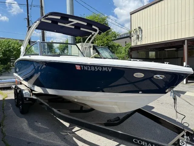 Slide: The Image of 2020 Cobalt CS23 boat on trailer, blue and white, parked outdoors. - 2