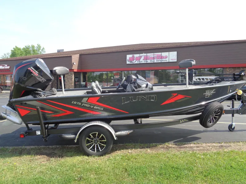 The Image of 2025 Lund 1875 Pro-V Bass XS boat on trailer, parked outside a marine store. - 0