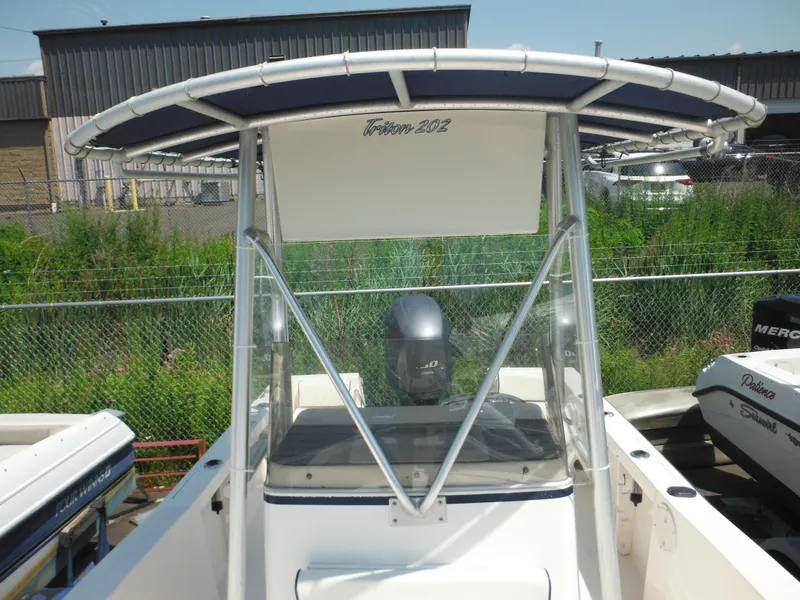 Slide: The Image of 2004 Sea Hunt 202 Triton boat with T-top and outboard motor, docked near greenery. - 18