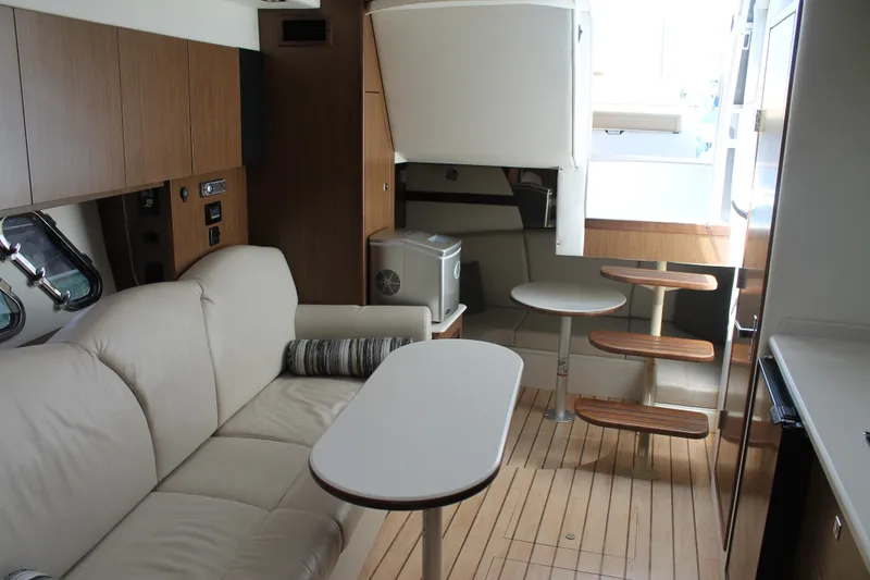 Slide: The Image of 2014 Cruisers Yachts 350 Express interior with beige sofa, wooden flooring, and compact dining area. - 49