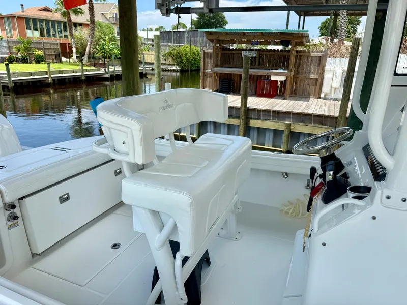 Slide: The Image of 2023 Regulator 23 boat interior with white seating and steering wheel, docked by a wooden pier. - 13