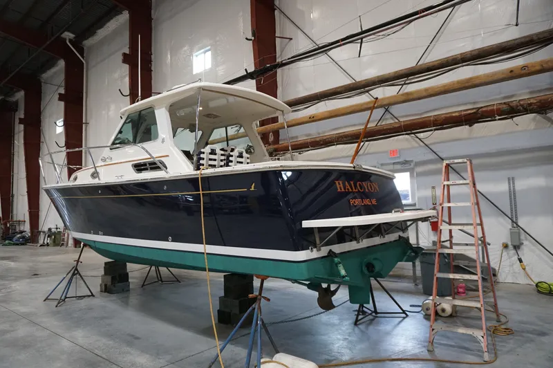 Slide: The Image of 2006 Back Cove 29 boat in a warehouse, elevated on blocks, with a ladder nearby. - 8