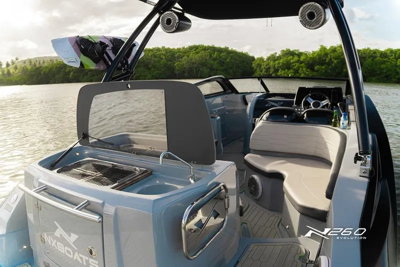 Slide: The Image of 2025 NX Boats NX260 EVOLUTION interior with seating and grill, set on a serene water backdrop. - 12