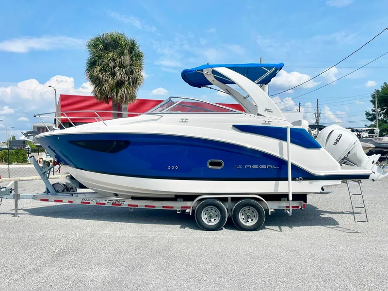 Slide: The Image of 2024 Regal 26XO boat on trailer, blue and white design, parked outdoors. - 1