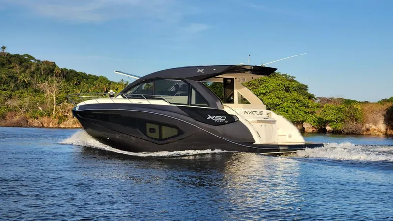Slide: The Image of 2025 NX Boats NX50 Invictus HT cruising on a serene river with lush greenery. - 7