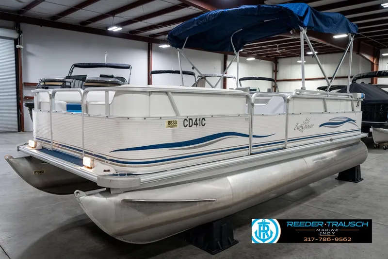 Slide: The Image of 2005 SunChaser 820 pontoon boat in indoor storage, featuring blue canopy and white exterior. - 2