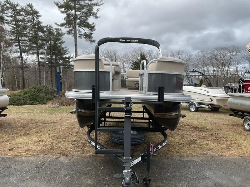 Slide: The Image of 2025 Sun Tracker PARTY BARGE® 18 DLX pontoon boat on trailer, parked outdoors. - 5