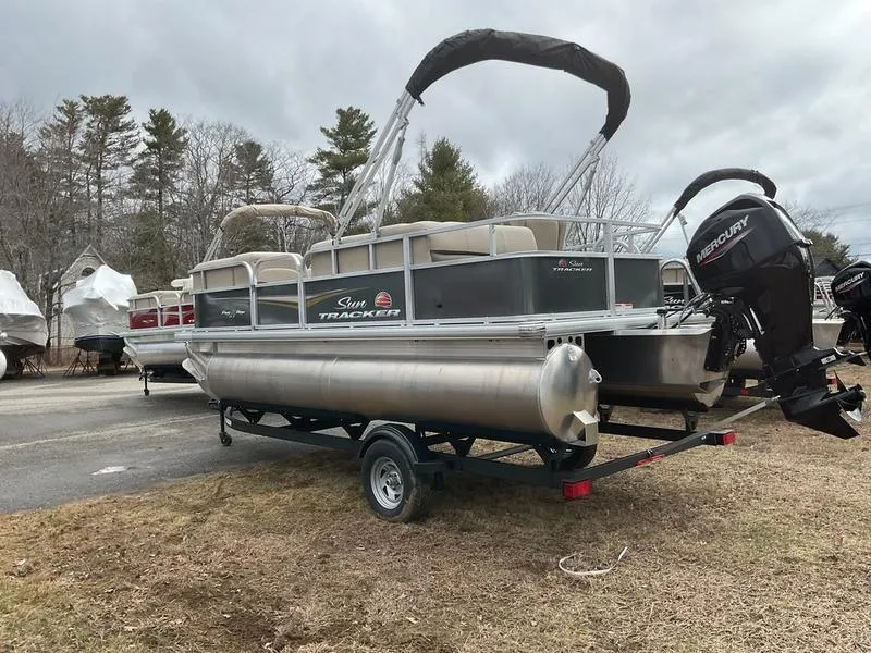 Slide: The Image of 2025 Sun Tracker PARTY BARGE® 18 DLX pontoon boat on trailer, parked outdoors. - 7