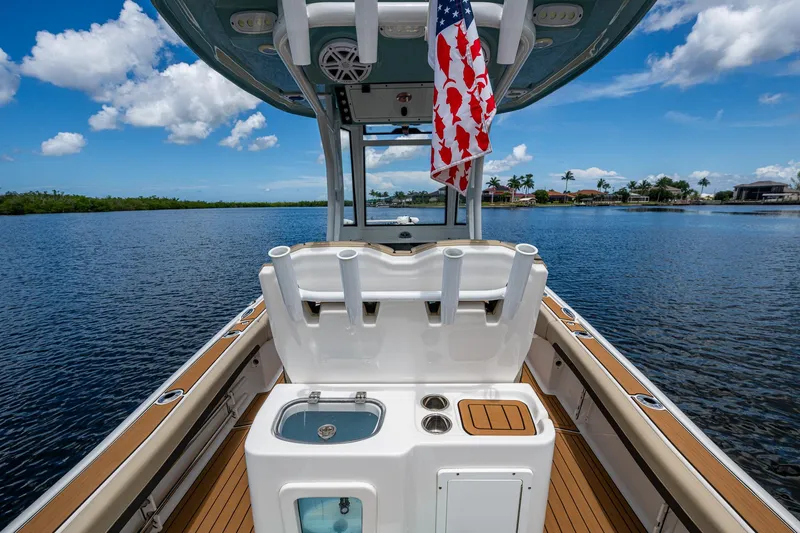 Slide: The Image of 2023 Tidewater 2700 Carolina Bay boat with fishing rod holders and American flag on calm water. - 36