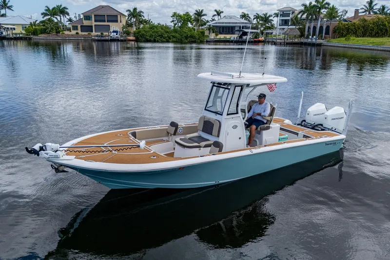 Slide: The Image of 2023 Tidewater 2700 Carolina Bay boat on calm water, surrounded by waterfront homes and palm trees. - 4