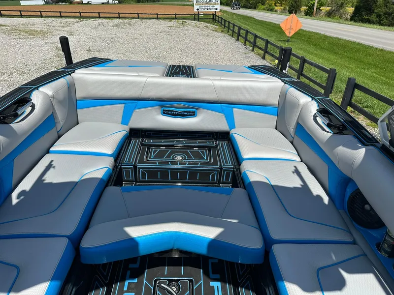 Slide: The Image of 2021 Centurion Fi25 boat interior with blue and gray seating, parked near a road. - 6