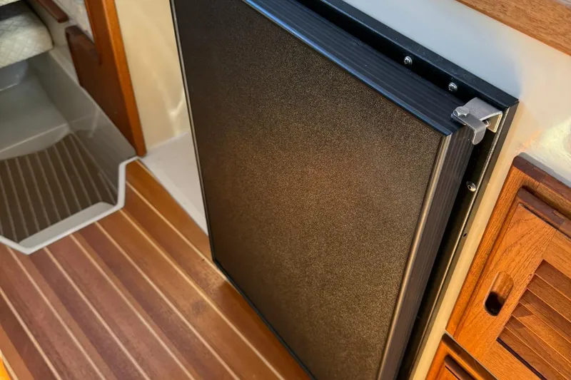 Slide: The Image of Interior of 2010 Ranger Tugs R-25 showing a compact refrigerator and wooden cabinetry. - 36