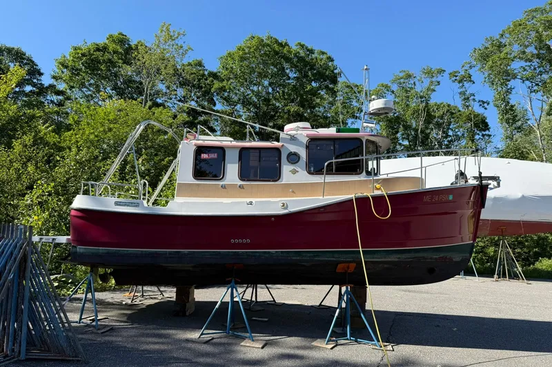 Slide: The Image of 2010 Ranger Tugs R-25 boat on stands, red hull, for sale, surrounded by trees. - 5