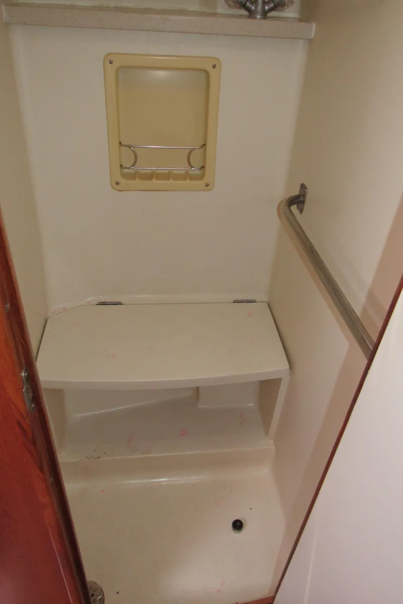 Slide: The Image of Compact shower area in a 2002 Hunter 466 boat, featuring a bench and grab bar. - 16