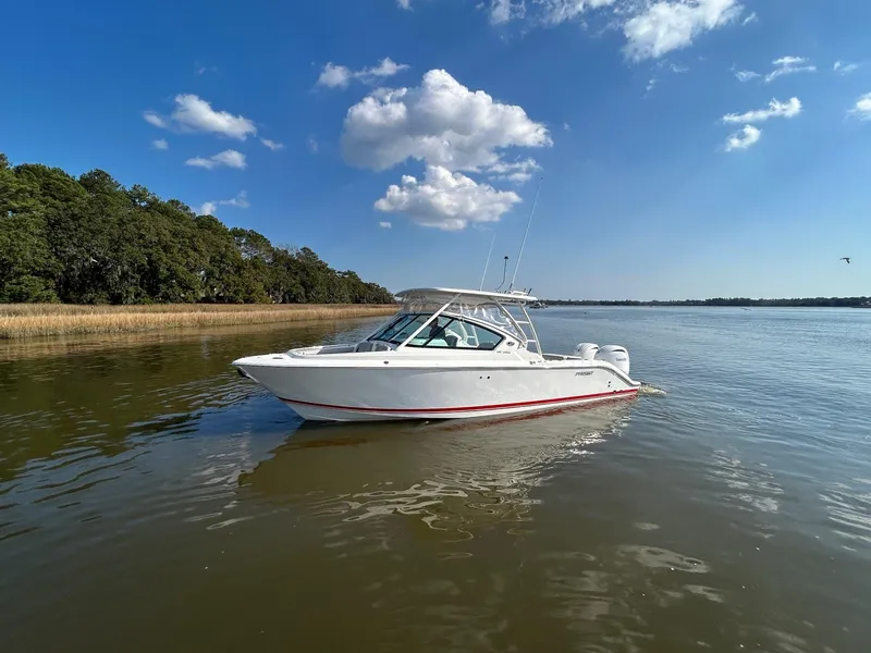 Slide: The Image of 2024 Pursuit DC 266 Dual Console boat on calm water under a clear blue sky. - 26
