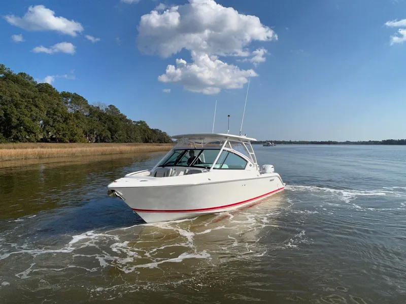 Slide: The Image of 2024 Pursuit DC 266 Dual Console boat cruising on a calm lake under a clear blue sky. - 31