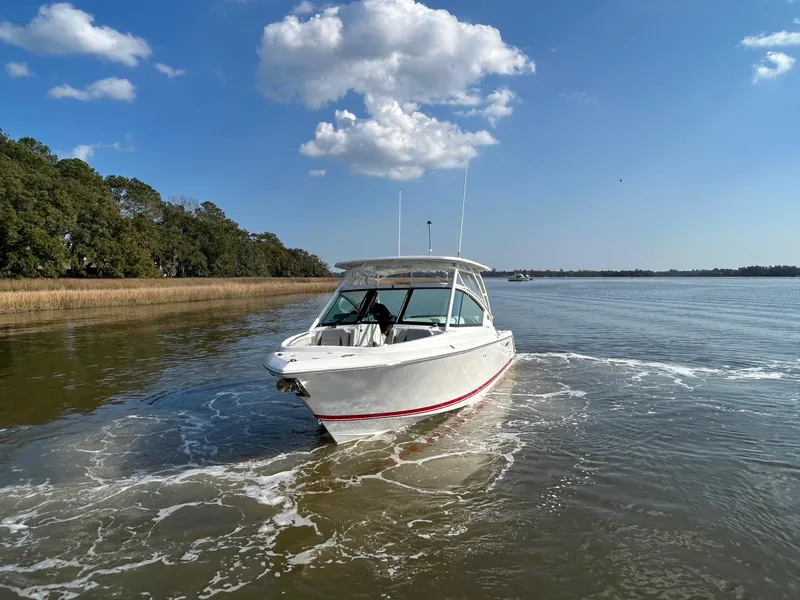 Slide: The Image of 2024 Pursuit DC 266 Dual Console boat cruising on a calm river under a clear blue sky. - 32