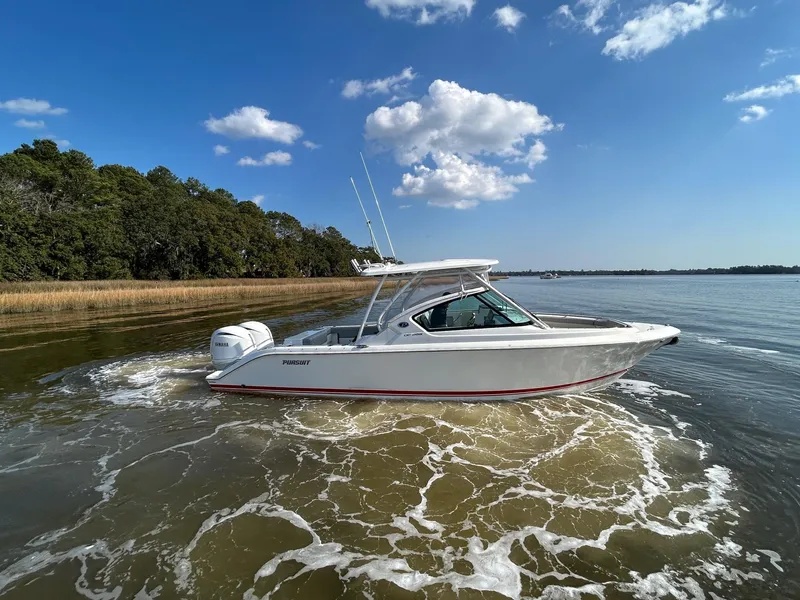 Slide: The Image of 2024 Pursuit DC 266 Dual Console boat cruising on a calm lake under a clear blue sky. - 34