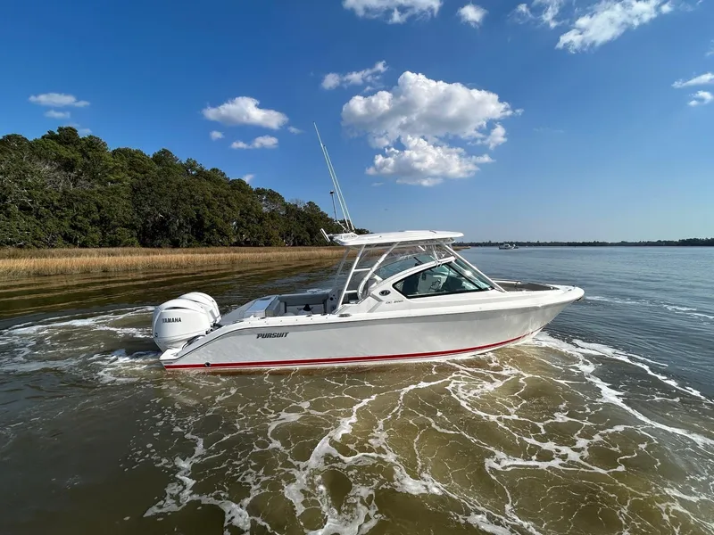 Slide: The Image of 2024 Pursuit DC 266 Dual Console boat cruising on a calm lake under a clear blue sky. - 36