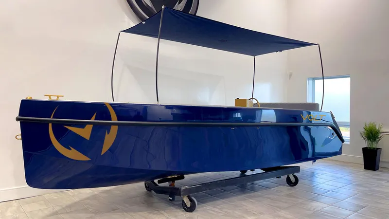 Slide: The Image of 2023 Vision Marine Technologies Volt 180 electric boat, blue with canopy, displayed indoors. - 18