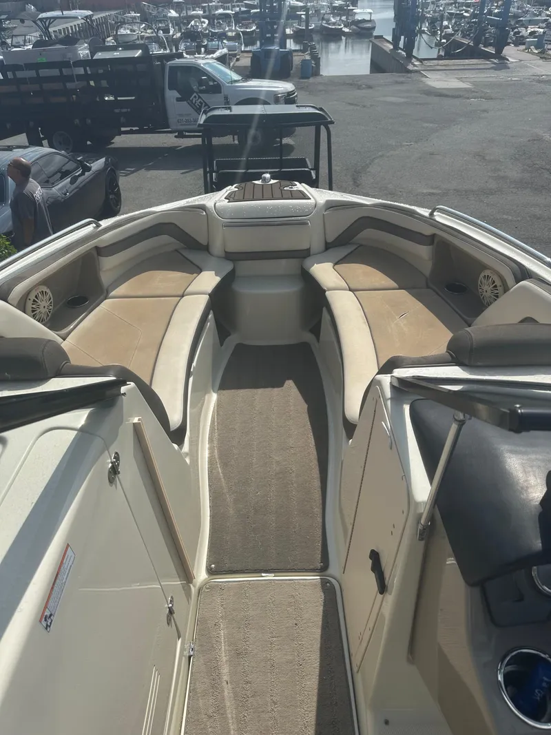 Slide: The Image of 2015 Yamaha Boats 242 Limited interior with beige seating and carpeted floor at a marina. - 10