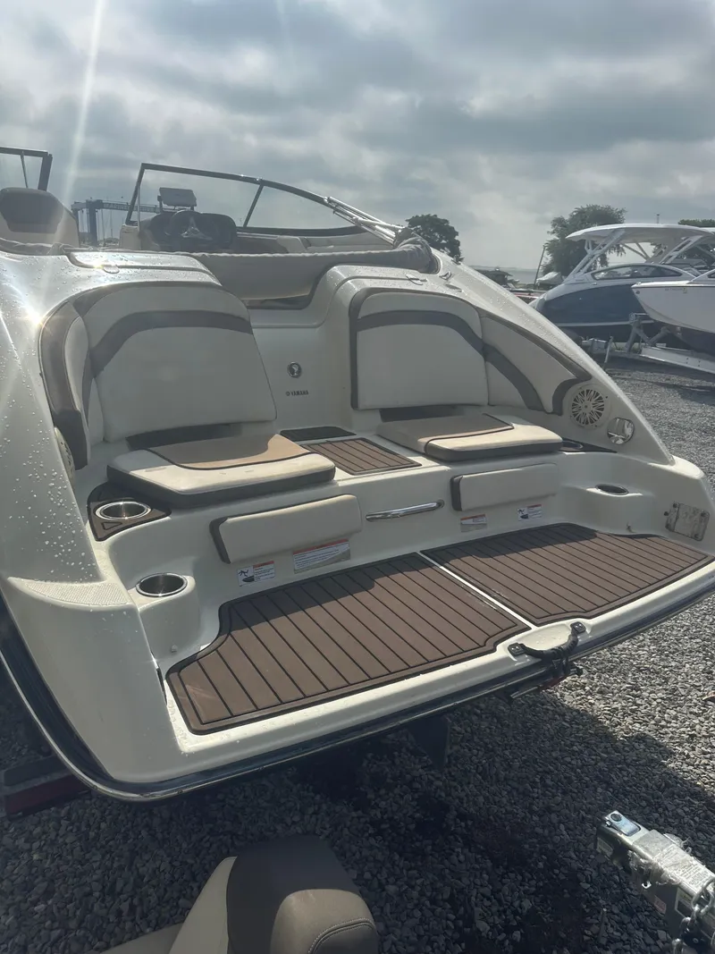 Slide: The Image of 2015 Yamaha Boats 242 Limited, rear view with seating and deck, parked on gravel. - 5
