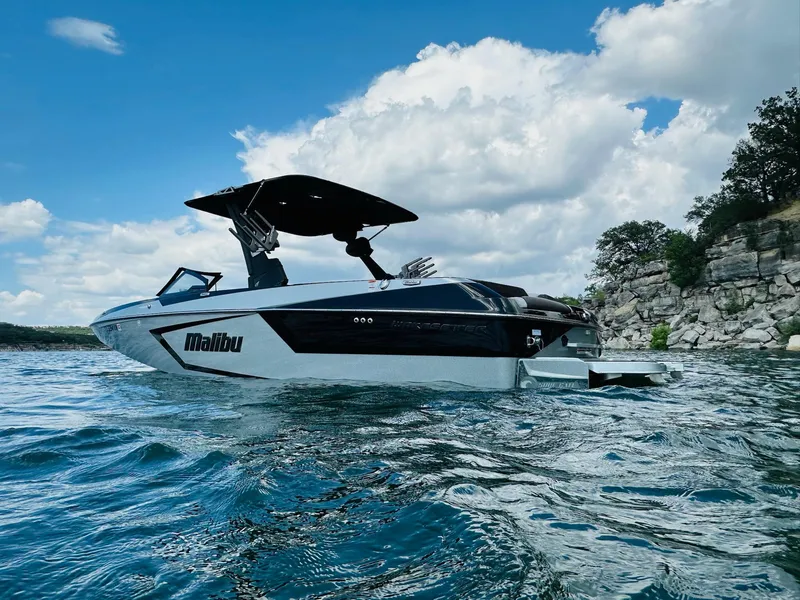 Slide: The Image of 2022 Malibu Wakesetter 24 MXZ boat on a scenic lake with rocky shoreline. - 2