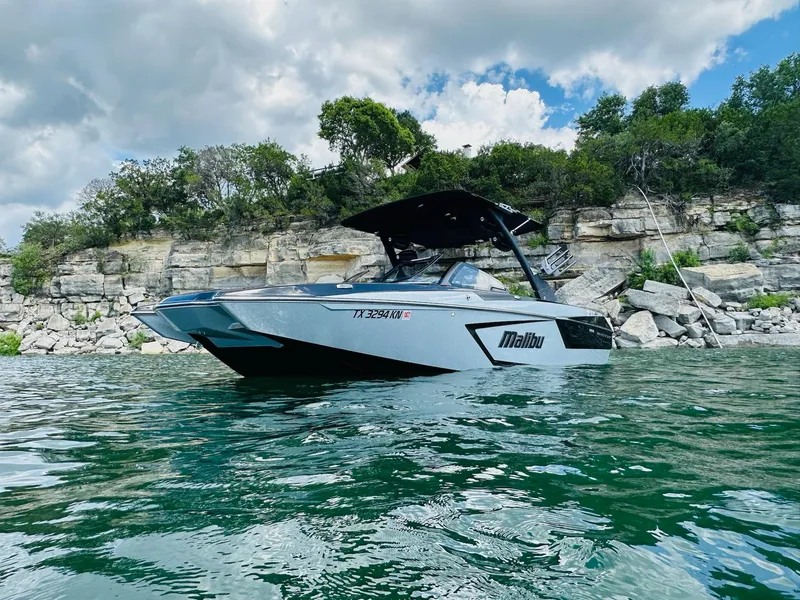 Slide: The Image of 2022 Malibu Wakesetter 24 MXZ boat on water, rocky shoreline background, cloudy sky. - 4