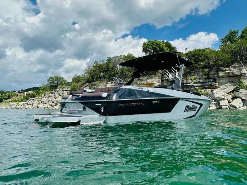 Slide: The Image of 2022 Malibu Wakesetter 24 MXZ boat on a scenic lake with rocky shoreline. - 5