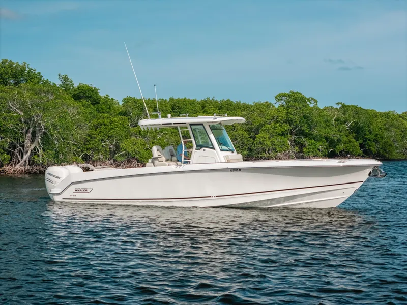 Slide: The Image of 2019 Boston Whaler 330 Outrage boat cruising on calm water near lush green shoreline. - 23