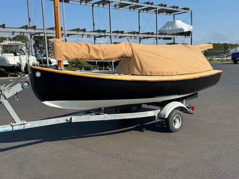 Slide: The Image of 2004 Custom Barnstable Cat Boat on trailer with tan cover in marina setting. - 1