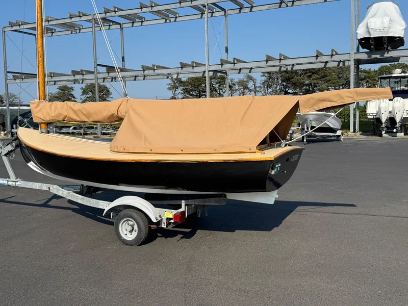 Slide: The Image of 2004 Custom Barnstable Cat Boat on trailer with tan cover in marina setting. - 2