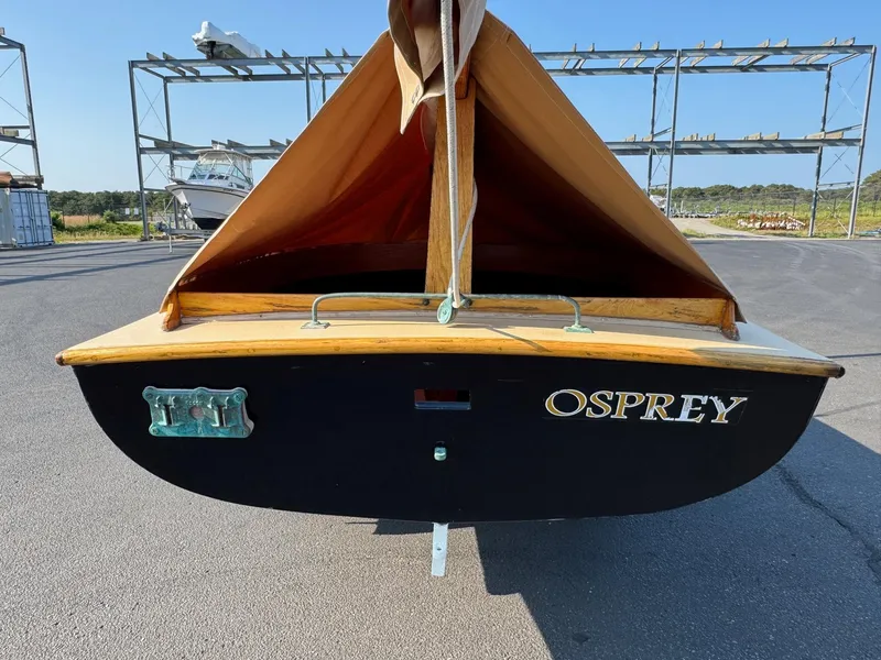 Slide: The Image of Custom 2004 Barnstable Cat Boat "Osprey" with tan sail, docked on asphalt. - 5