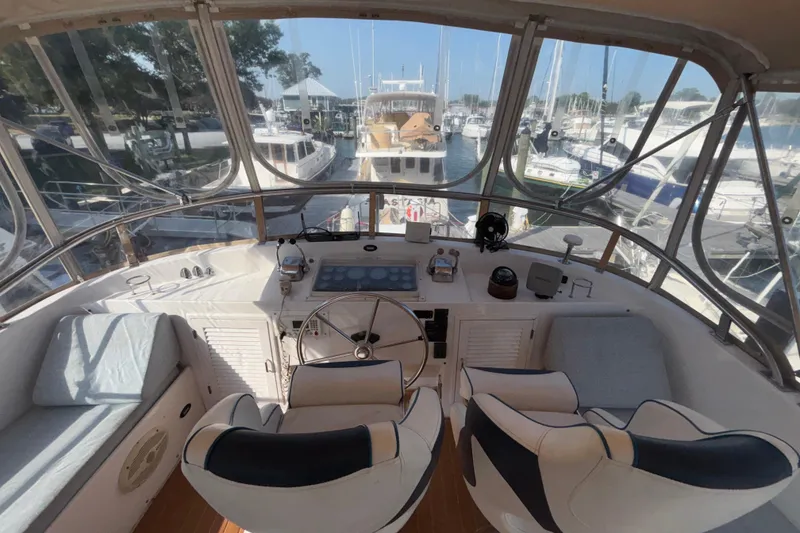 Slide: The Image of 1989 Jefferson 42 Sundeck Motor Yacht helm with marina view, featuring dual seats and navigation controls. - 26