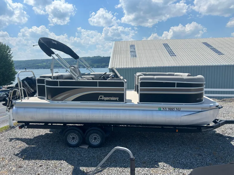 Slide: The Image of 2014 Premier 220 SunSation pontoon boat on trailer, parked near a lake under a cloudy sky. - 29