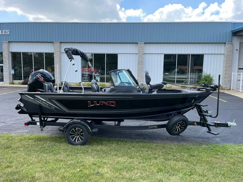 The Image of 2026 Lund 1775 Impact XS Sport boat on trailer, parked outside dealership. - 0
