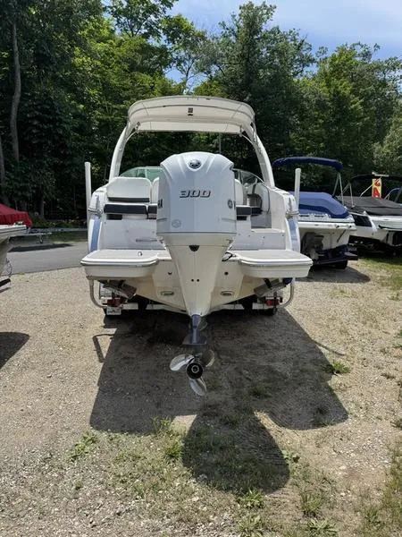 Slide: The Image of 2020 Regal 26 OBX boat, rear view, parked on gravel, surrounded by trees and other boats. - 2