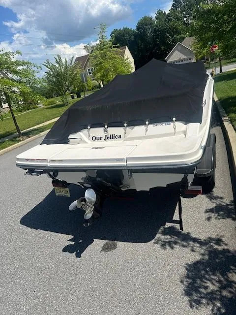 Slide: The Image of 2018 Sea Ray SPX 230 boat with cover, parked on a sunny residential street. - 2