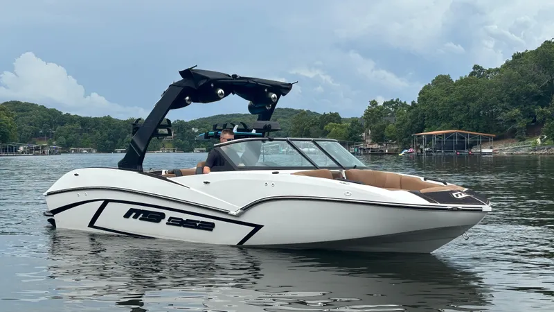 Slide: The Image of 2025 MB B52 23 Alpha boat on a calm lake with lush green shoreline. - 2