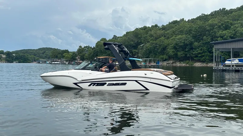 Slide: The Image of 2025 MB B52 23 Alpha boat on a lake, surrounded by lush greenery and docks. - 3