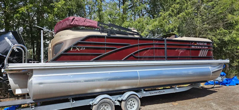 The Image of 2022 Bennington LX 23 Quad Bench pontoon boat on trailer, surrounded by trees. - 1