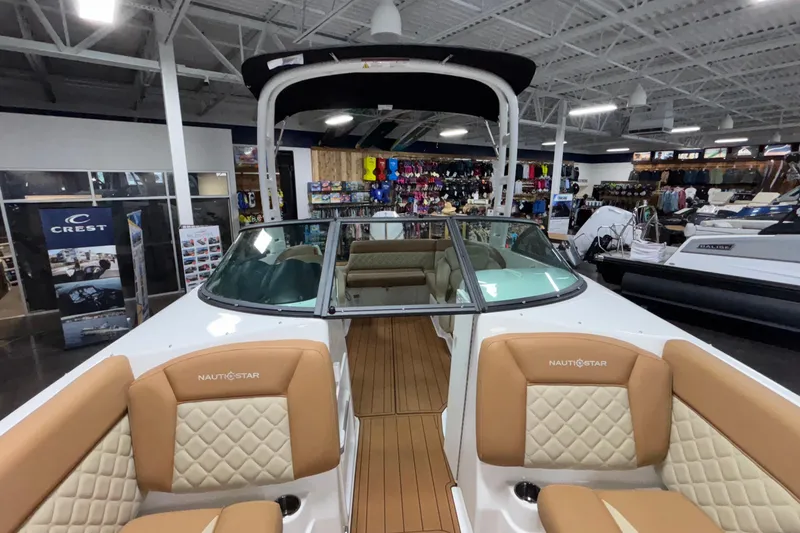 Slide: The Image of 2025 NauticStar 243 DC Deck boat interior with tan seating in showroom. - 14