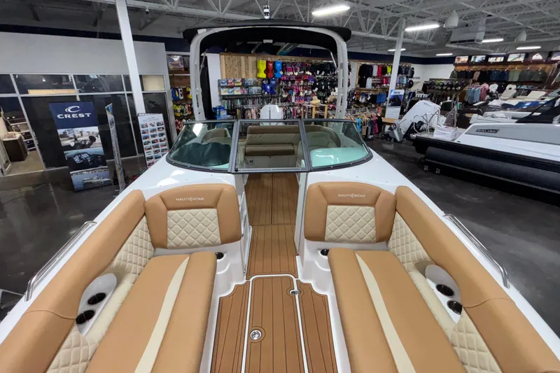 Slide: The Image of 2025 NauticStar 243 DC Deck boat with tan seating in showroom. - 18