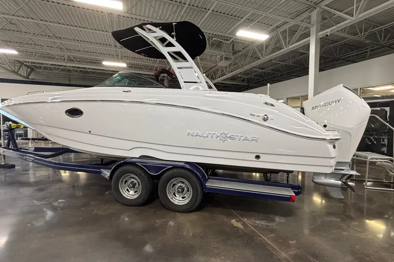 Slide: The Image of 2025 NauticStar 243 DC Deck boat on trailer in showroom, side view. - 25