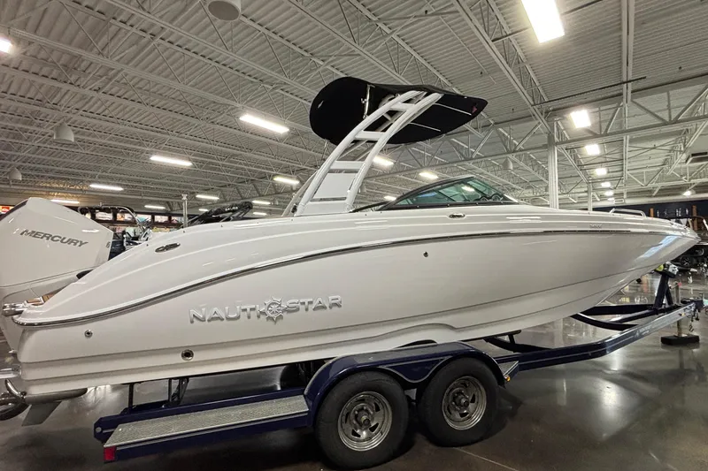 Slide: The Image of 2025 NauticStar 243 DC Deck boat on trailer in showroom, side view. - 28