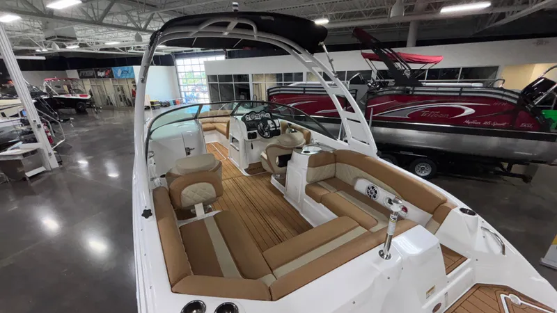 Slide: The Image of 2025 NauticStar 243 DC Deck boat interior with tan seating and modern dashboard in showroom. - 6