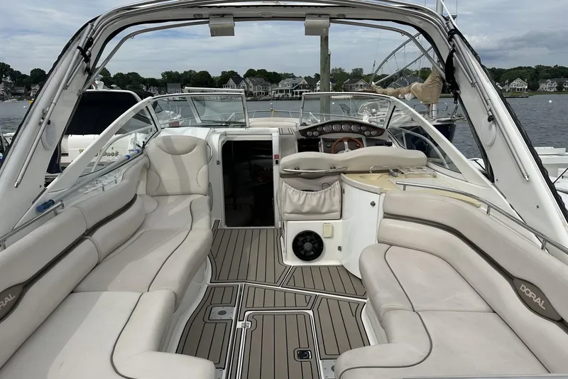 Slide: The Image of 2002 Doral 330se boat interior with beige seating and wood accents, docked by a scenic waterfront. - 4