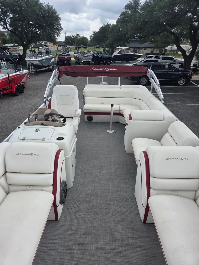 Slide: The Image of 2017 South Bay 523 CR pontoon boat with white seating and red accents, parked outdoors. - 5