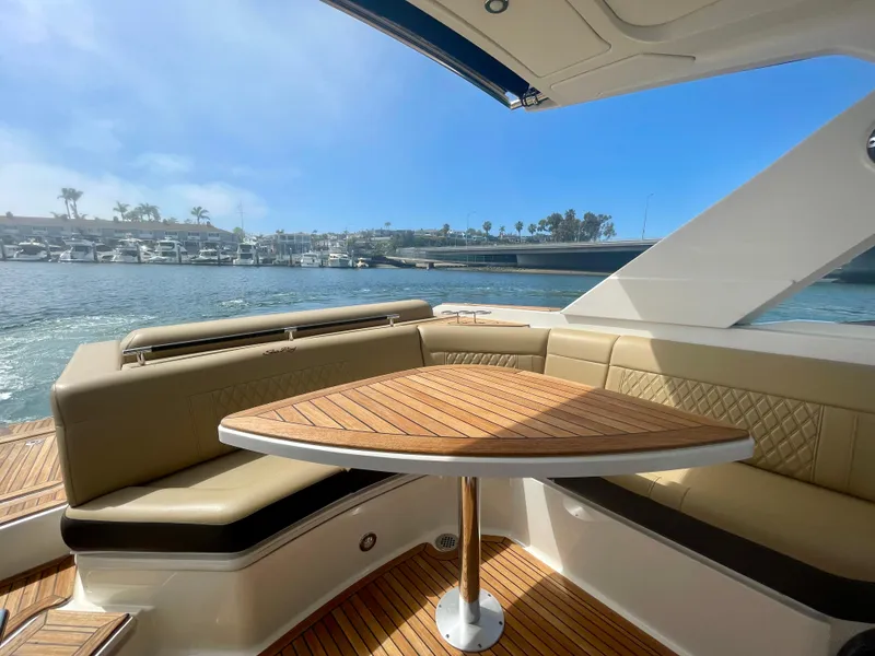 Slide: The Image of 2019 Sea Ray SLX 310 boat interior with elegant seating and wooden table, overlooking marina. - 14